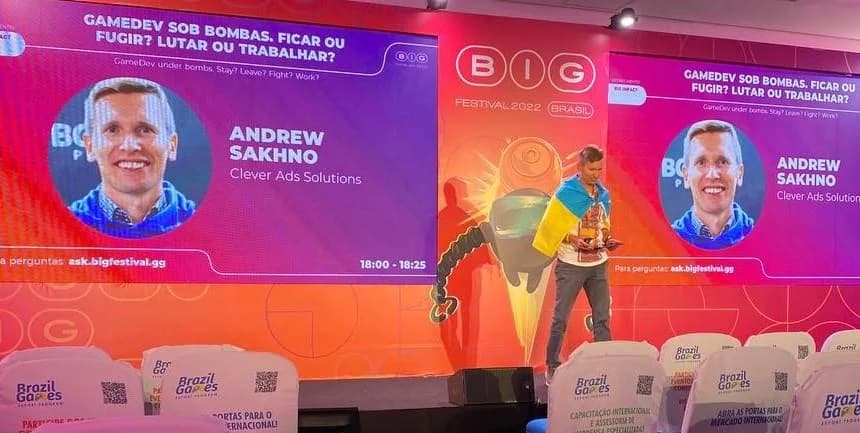 Andrew Sakhno on stage at BIG Festival, a Ukrainian flag over his shoulders, his name and the talk title on both screens