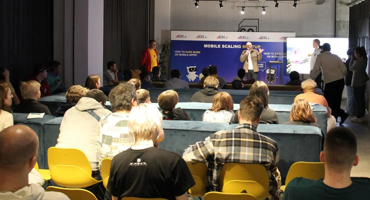 A full hall facing the stage, the speaker in front of the “Mobile Scaling Meetup” screen